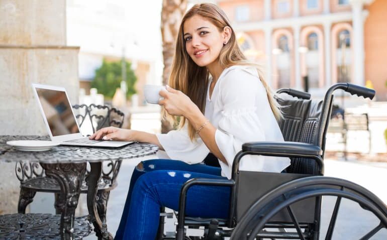Mulher de cadeira de rodas tomando café e usando computador