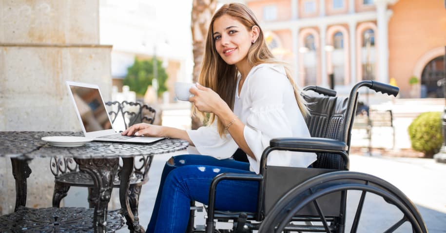 Mulher de cadeira de rodas tomando café e usando computador